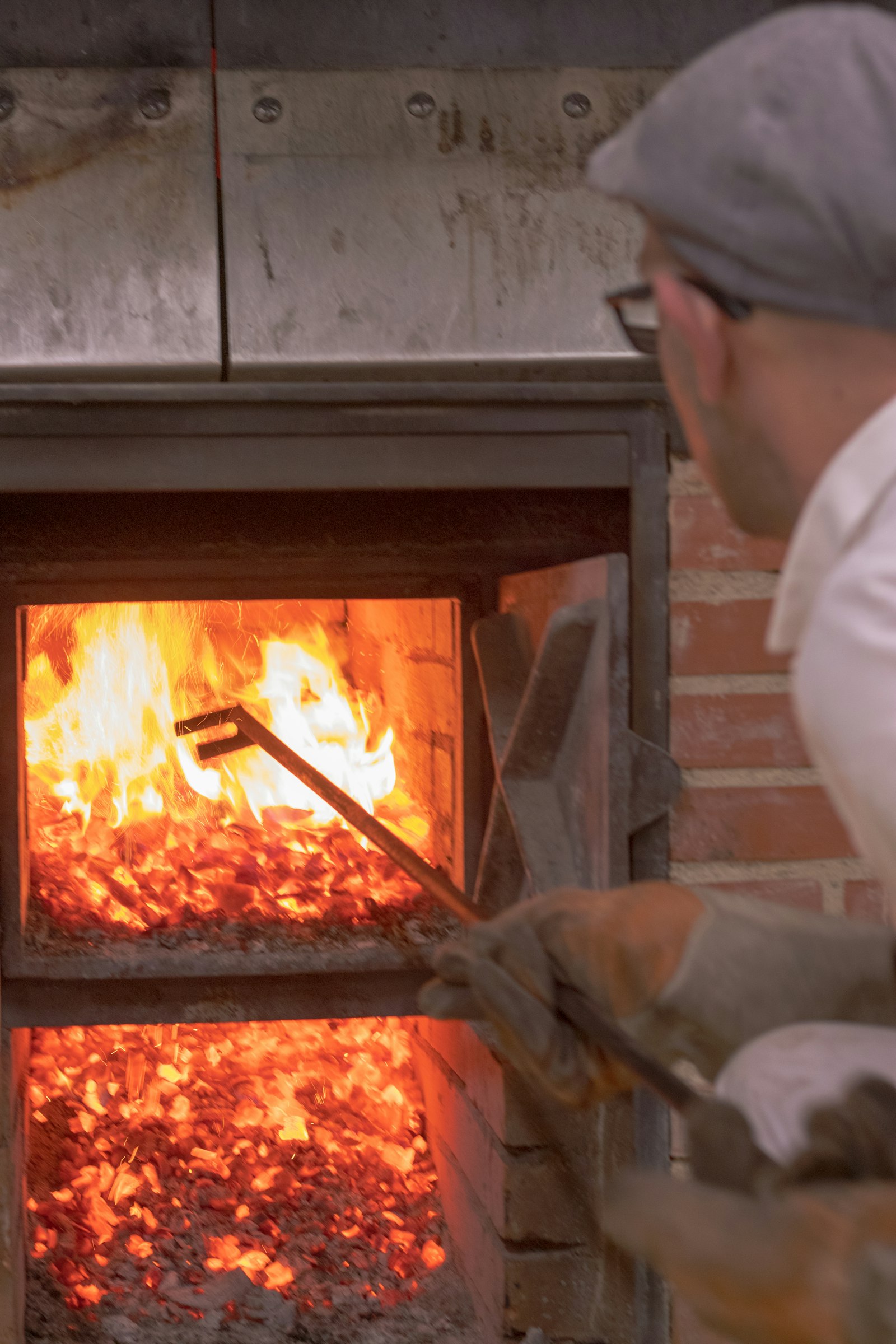 A baker working the wood-fired hearth with a long peel