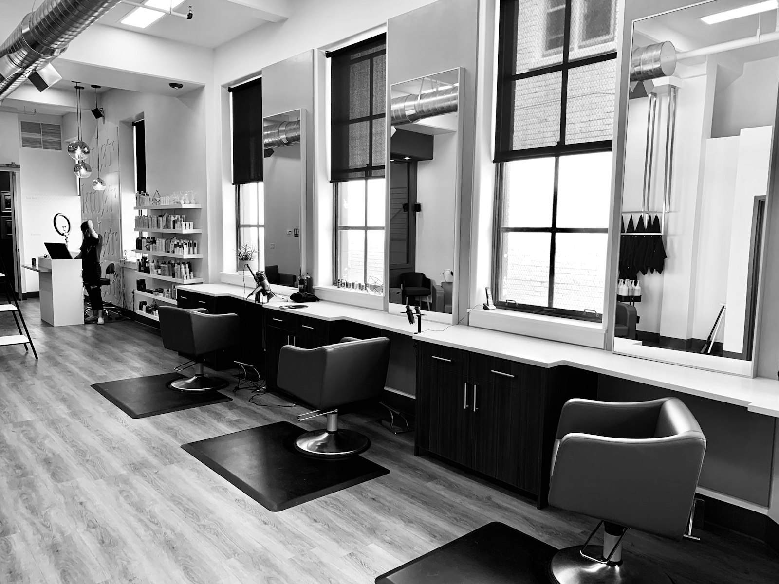 A student near three salon chairs on the practical floor between client appointments.