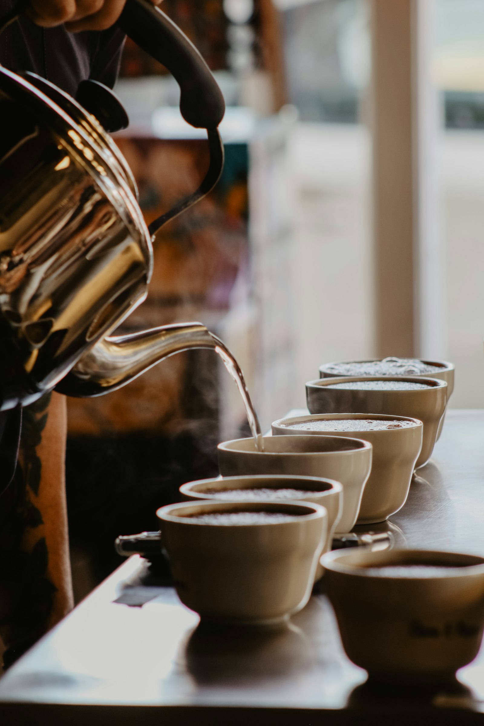 Pouring hot water into a row of cupping bowls during a Friday cupping session