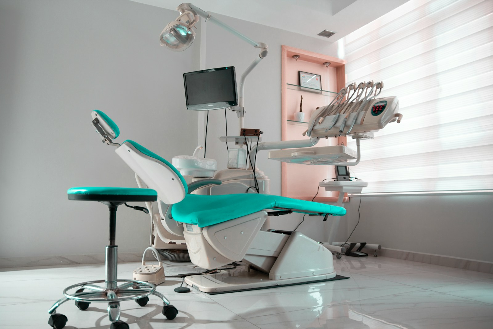 A modern dental treatment room with a chair, monitor, and overhead light, set up for a visit.
