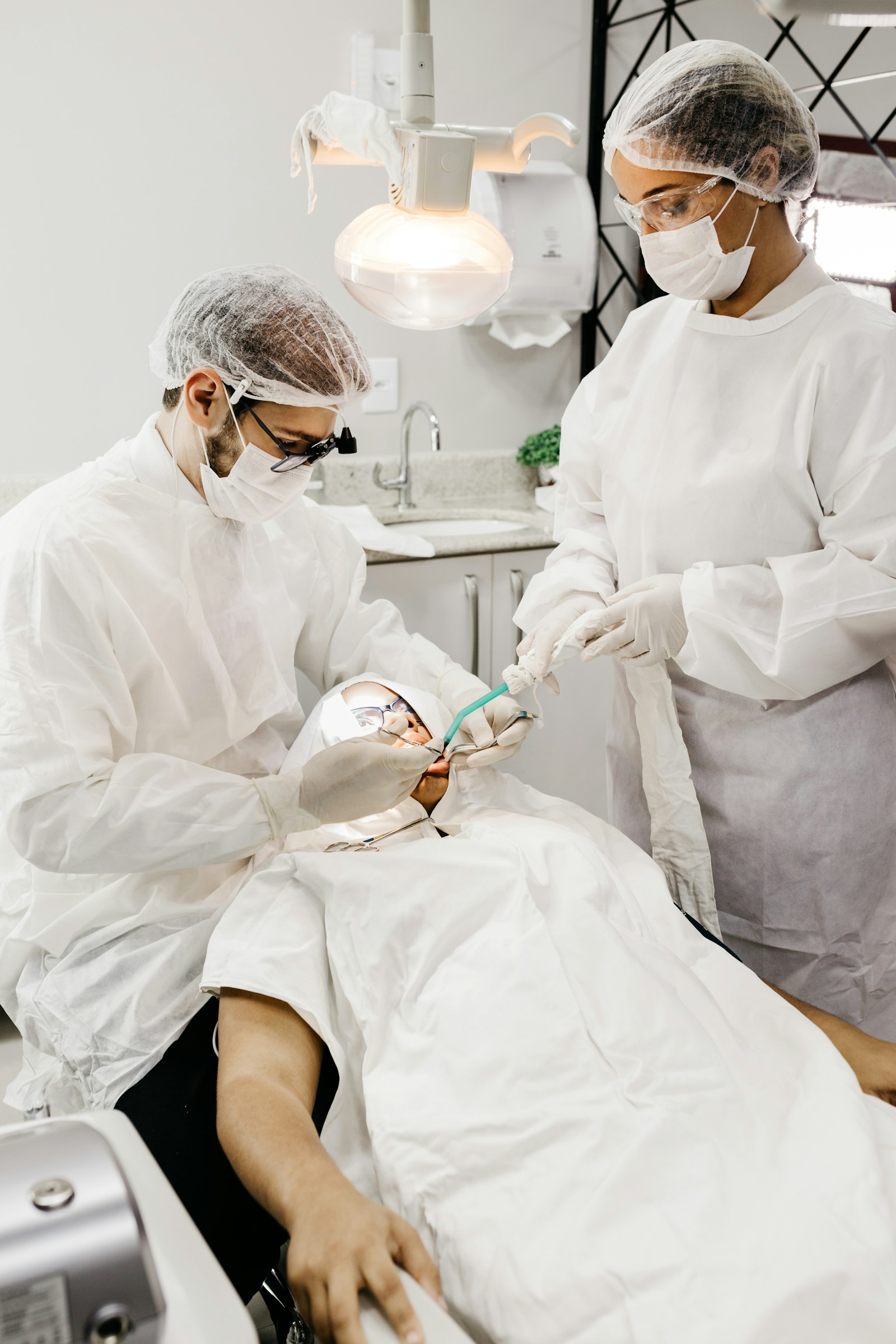 A hygienist in scrubs working with a suction tool, hands at work in a treatment room.