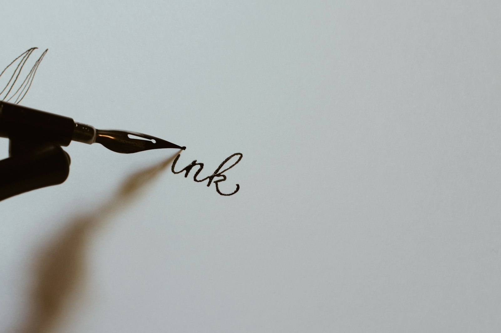 Close-up of a hand holding a black fountain pen writing on white paper.