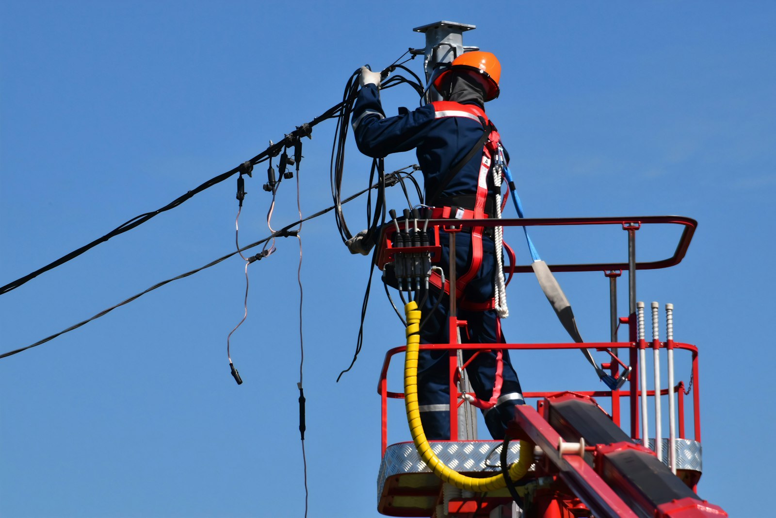 Electrician in red jacket and orange helmet wiring an overhead panel