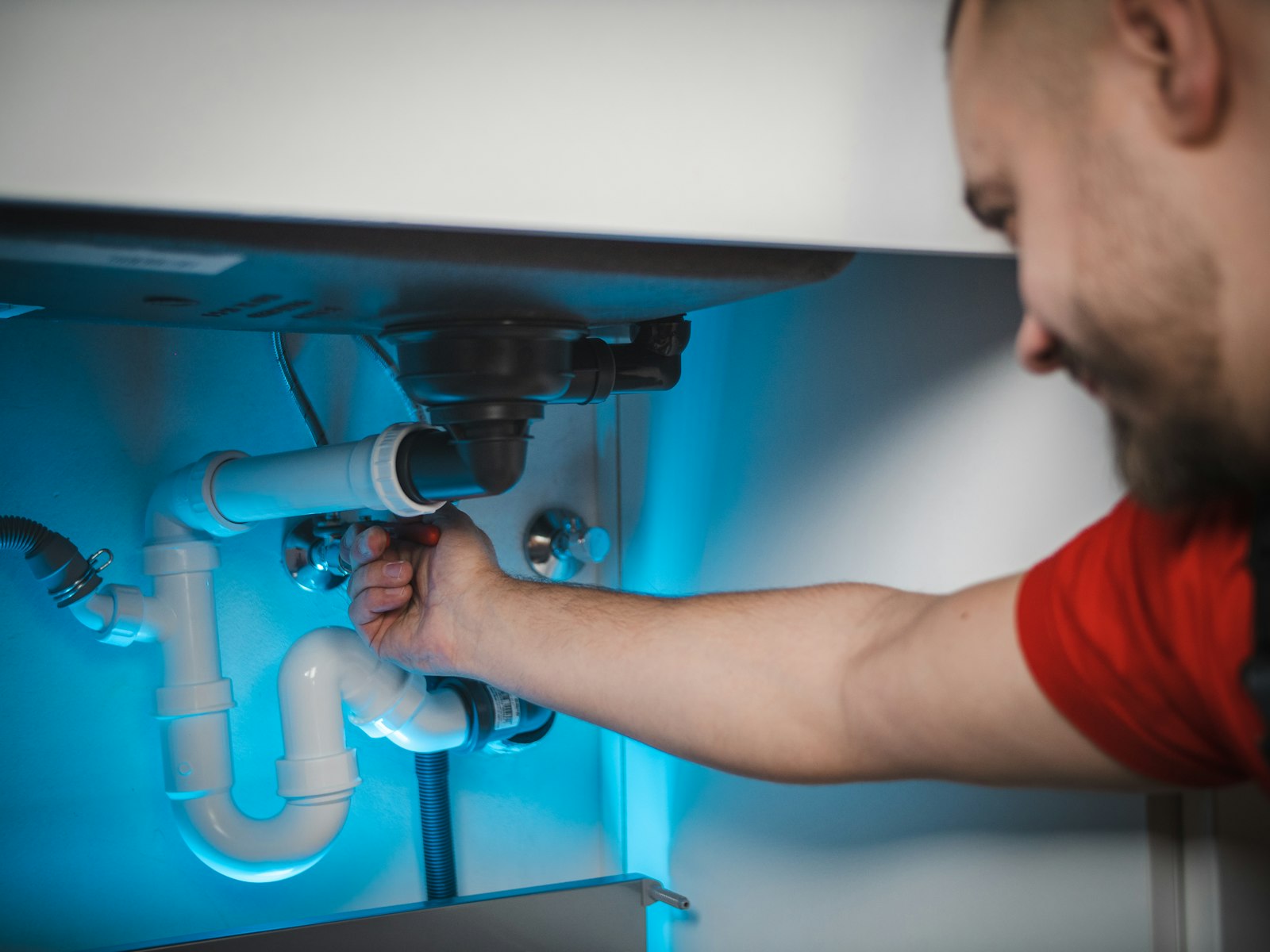 Plumber kneeling at a cabinet, working on copper pipe with both hands
