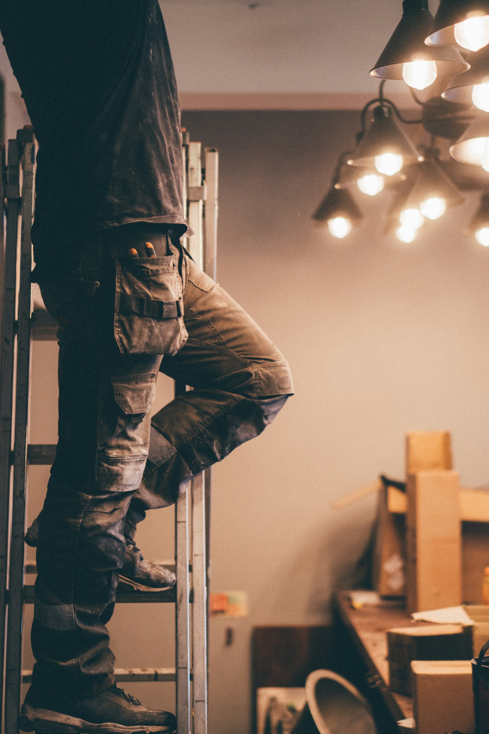 Electrician on a step ladder running new conduit in a job-site ceiling