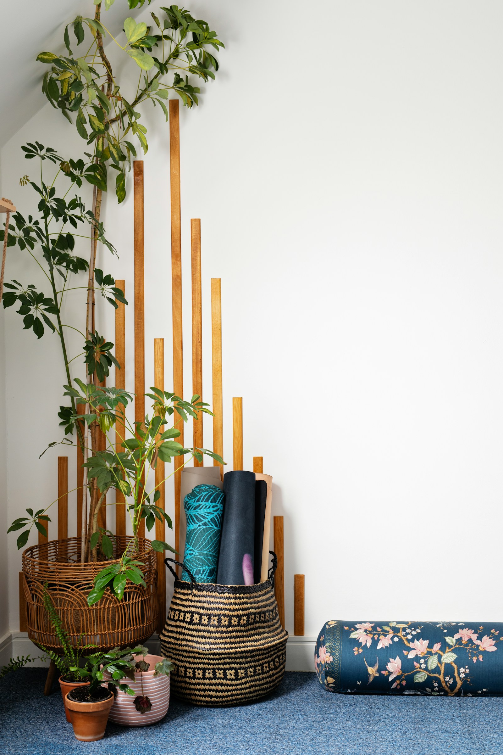 Rolled yoga mats stacked against a wall beside potted plants in a quiet studio corner