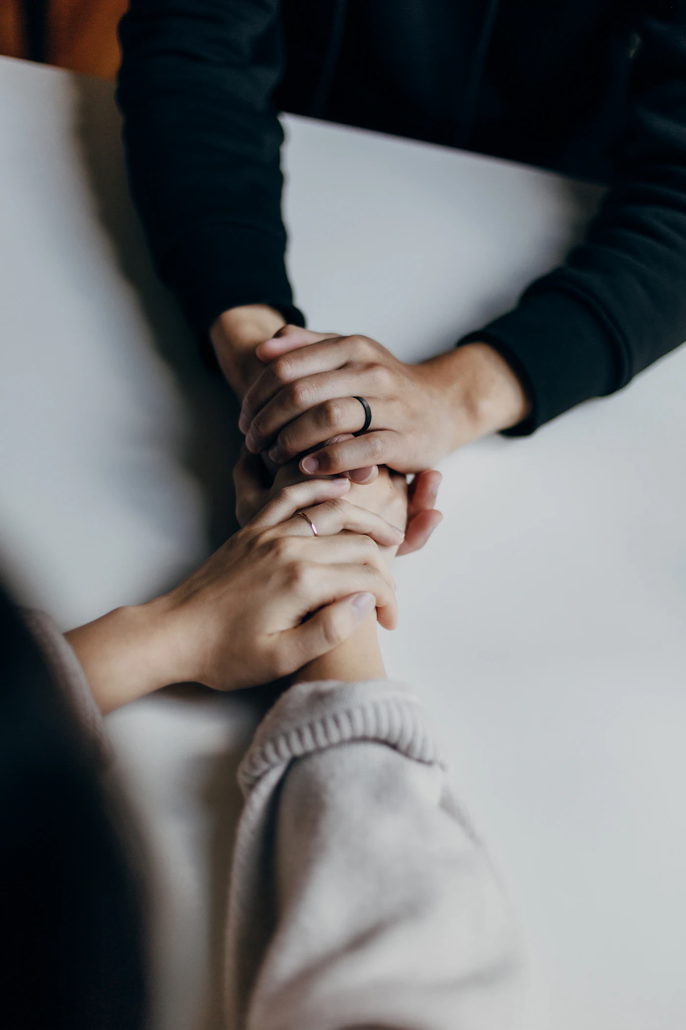 Two pairs of hands resting on a table, holding each other gently.