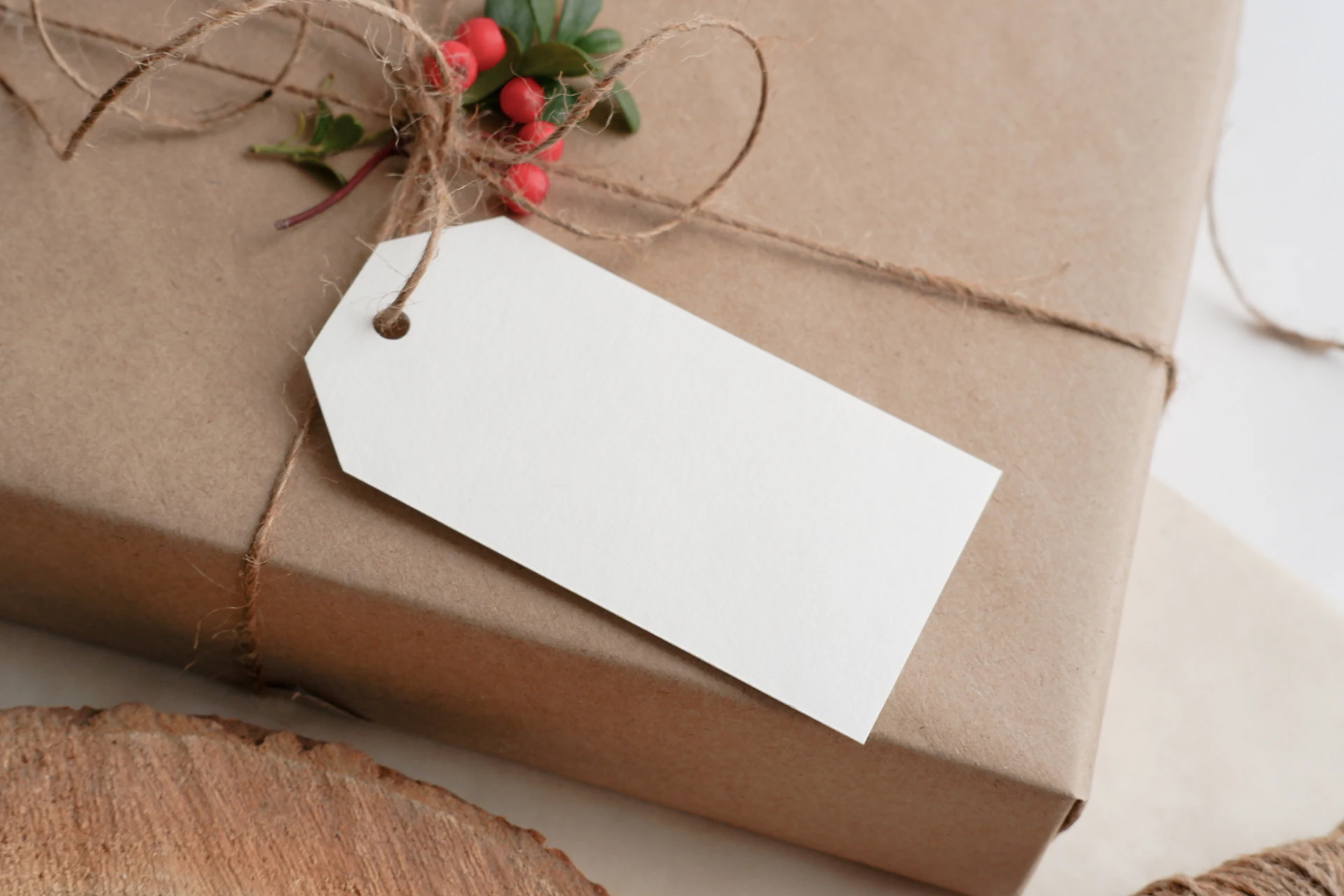 A present wrapped in brown paper and tied with twine, with a blank gift tag and a sprig of red berries.