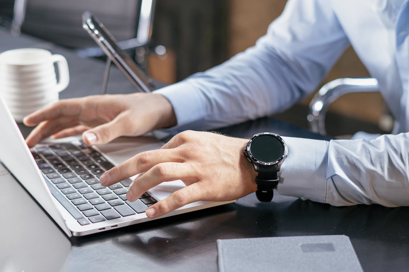 A person working at a laptop with a notepad and coffee nearby.