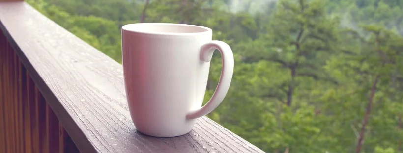 Get a head start. A mug kept on a railing with trees in the background.