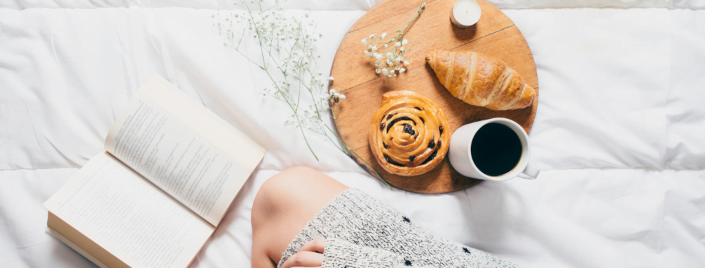 Lady reading a book with a breakfast platter consisting of breads and coffee
