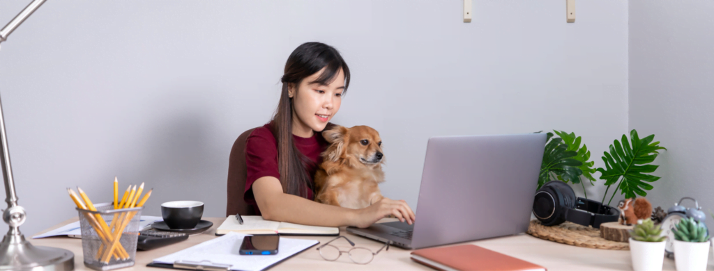 Girl typing on her laptop with her dog seated on her lap.