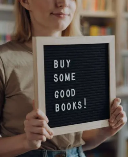 A blond-haired woman holding a letter board that reads "Buy some good books!"