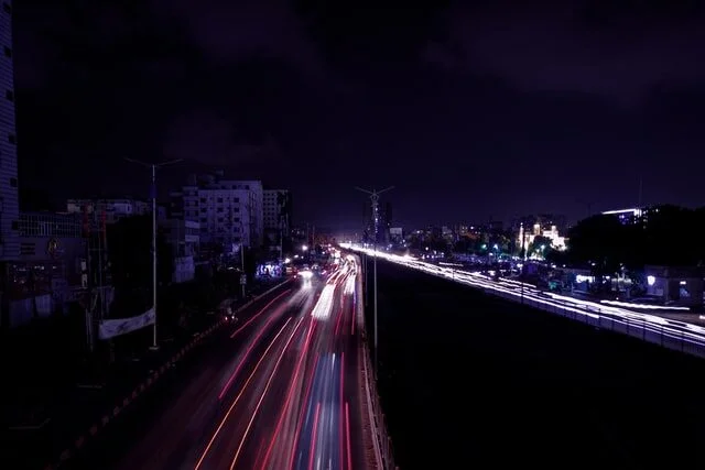 A long-exposed photo of a city road at night, showing a trail of lights from cars.