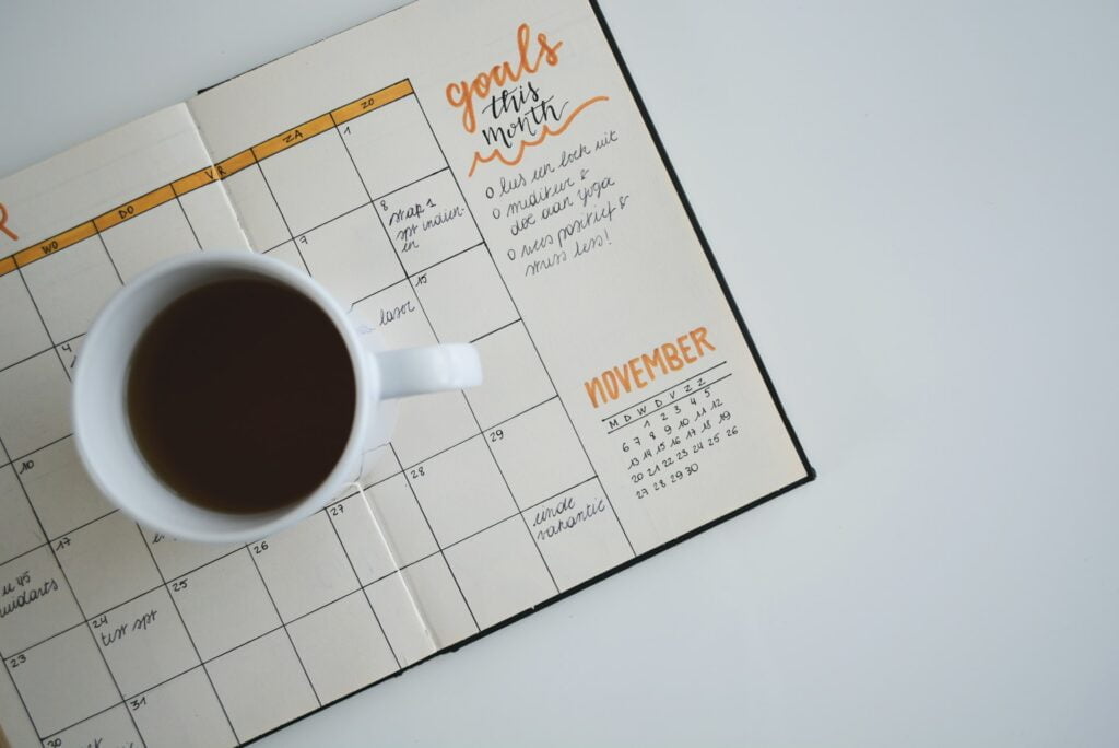 Filled coffee mug kept on top of a full-page wide calendar within a journal.
