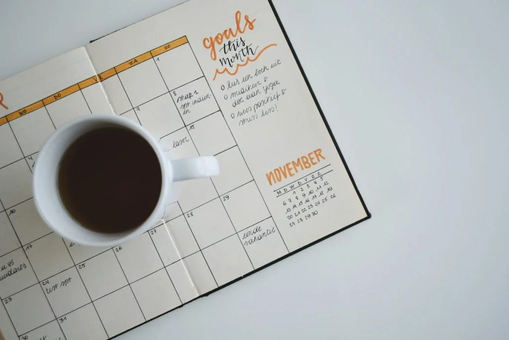 Filled coffee mug kept on top of a full-page wide calendar within a journal.