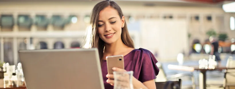 A woman looking at her phone while also using her laptop.