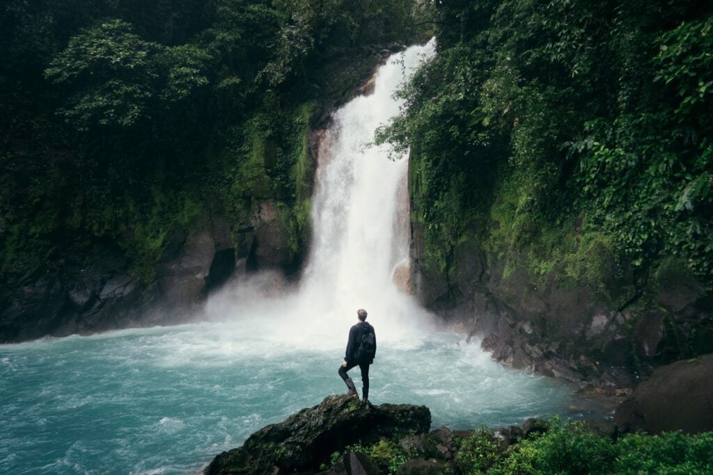 Man standing on cliff near falls.