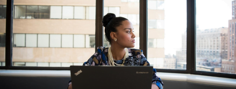 Think before you act A woman working on her ThinkPad laptop, looking outside the giant windows.
